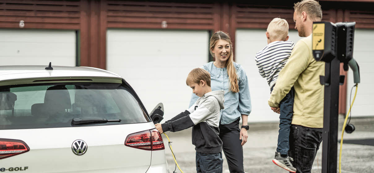 Familj som står vid en elbil. Sonen håller i en laddkabel och laddar bilen.