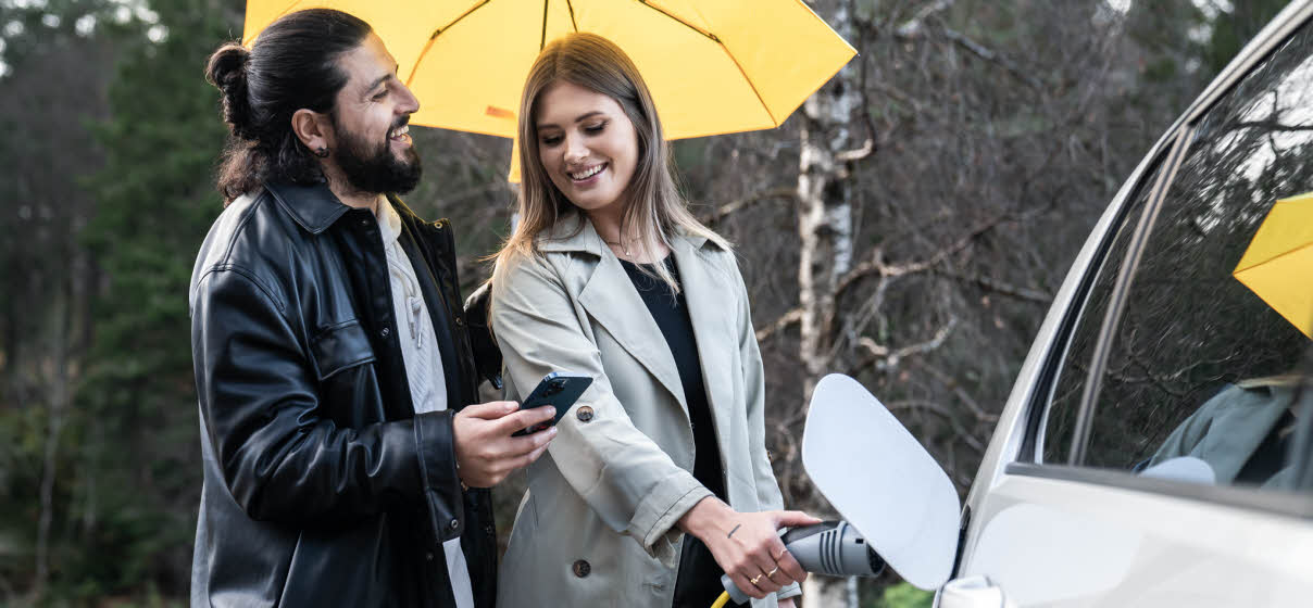 en kvinne som holder en elbillader og en mann som holder en gul paraply og en mobiltelefon