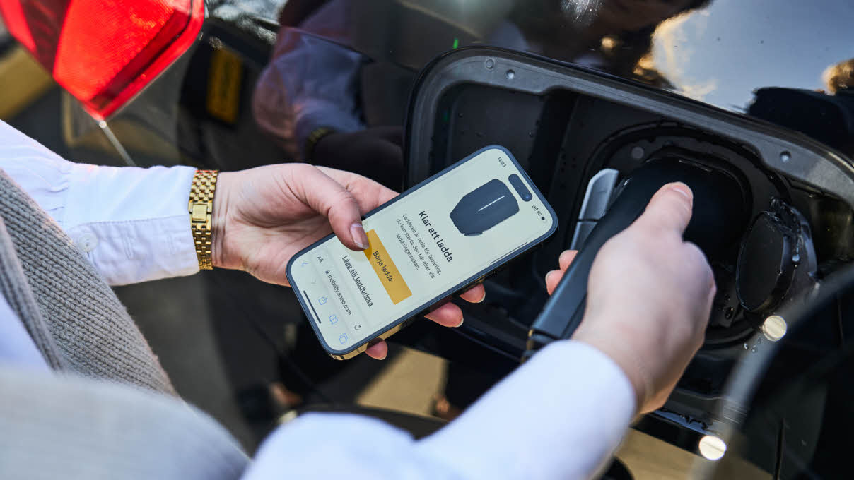 Kvinna sätter in laddkabel i elbil och börjar ladda med mobiltelefon