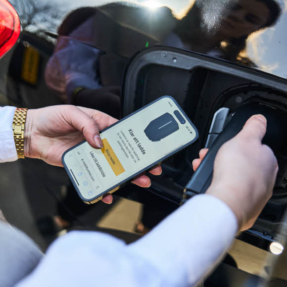 Kvinna sätter in laddkabel i elbil och börjar ladda med mobiltelefon